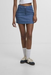 Denim mini hameva keskisinisena, millel on tagasihoidlik disain, esine nupuga kinnitamine ja kaks taskut. Kombineeritud valgete sokkide ja tennisetossudega.