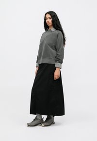 Šedá mikina s pruhovaným golierom, nosená cez dlhú čiernu sukňu. Šedé turistické topánky s tmavými šnúrkami dopĺňajú outfit.