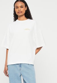 Λευκό oversized t-shirt κατασκευασμένο από βαμβάκι, με κοντά μανίκια και κεντημένο λογότυπο "Barbour International" σε χρυσό μπροστά.