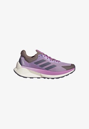 Lilla og brun Adidas Terrex løbesko med sorte striber, pink snørebånd og en tyk hvid sål designet til trail brug.