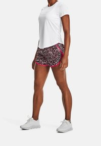 Vit kortärmad träningsskjorta kombinerad med flerfärgade mönstrade shorts med rosa detaljer, samt ljusgrå träningsskor.