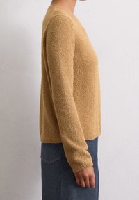 Beige textured sweater with long sleeves and a round neckline, featuring a boxy shape and ribbed hem, paired with a denim skirt.