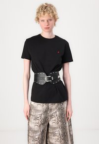 Sort bomulls T-skjorte med en liten rød logo. Brukt med et bredt svart lærbelte dekoret med sølvnagler og en dekorativ spenne over mønstrede bukser.