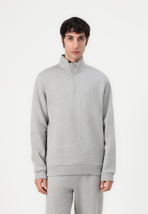 Sudadera de cuello con cremallera en gris claro, fabricada en un tejido suave, de mangas largas, con puños y dobladillo acanalados, diseño minimalista con un sutil logotipo en el pecho.