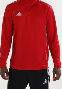 Rood sportief langmouwshirt met een halve rits kraag, witte streepdetails en het Adidas-logo op de linkerkant van de borst.