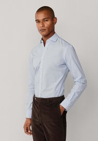 Lichtblauw overhemd met knopen en een subtiel patroon, lange mouwen en een kraag, gecombineerd met donkerbruin corduroybroeken.