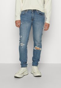 Jeans decolorate, de un albastru deschis, cu detalii rupte, croială dreaptă, din material de bumbac, asortați cu adidași albi cu glezna înaltă.