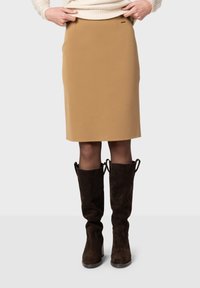 Jupe en crêpe marron avec une texture lisse, longueur mi-mollet, et poches latérales, associée à des bottes en suède marron montantes avec des lacets.