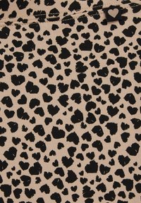 Bež tkanina s nepravilnim crnim mrljama u obliku srca i mala crna oznaka s bijelim srcem blizu šava.