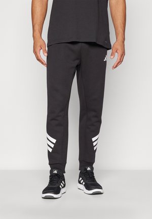 Pantaloni jogger neri in cotone con gamba affusolata, caratterizzati da accenti bianchi a tre righe sulla parte inferiore delle gambe e polsini a coste alle caviglie.