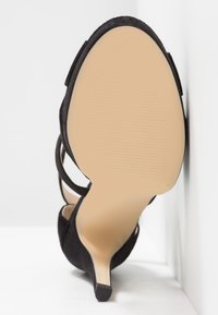 Chaussure à talons hauts en daim noir avec un bout pointu, un talon fin et une semelle beige lisse avec une texture ridée pour une meilleure adhérence.