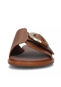 Sandali slide in pelle marrone con punta aperta e una larga fascia decorata con una fibbia circolare in argento. Suola piatta e texture.