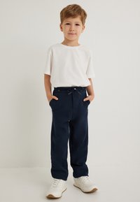 Hvid kortærmet t-shirt parret med marineblå drawstring-bukser og hvide sneakers. Outfittet har et enkelt, afslappet design.
