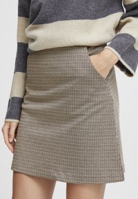 Houndstooth-patterned mini skirt in beige and brown, featuring a side pocket and a fitted silhouette, complemented by a knitted top.