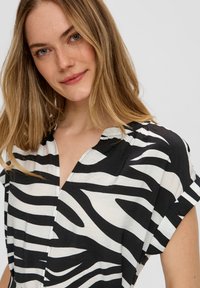 Zebra-gestreepte zwart-witte shirt met een v-hals, korte opgerolde mouwen en een lichte, iets gekreukte stofstructuur.