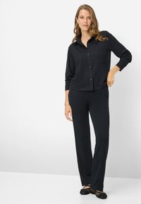 Sort loungewear-sæt med en skjorte med knapper og lomme samt afslappede bukser. Glat stof med lange ærmer og afsluttede kanter.