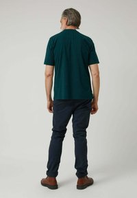 Camiseta de algodón verde con mangas cortas, cuello redondo y corte recto, combinada con pantalones oscuros de color marino y calzado marrón.