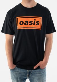 Black cotton t-shirt featuring a large orange rectangular logo with the text "oasis" in bold black letters across the chest.