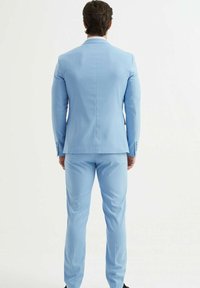 Costume bleu clair au design ajusté, avec une fente unique à l'arrière, un pantalon slim et des accents de boutons sur les poignets.
