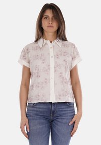 Blusa a maniche corte in crema con stampa floreale rosa chiaro, dotata di bottoni frontali e colletto, realizzata in un tessuto leggero.