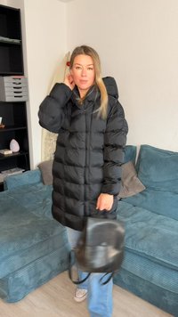 Giacca imbottita nera con cappuccio, design trapuntato e zip frontale. Indossata sopra jeans azzurri chiari e abbinata a una piccola borsa nera.