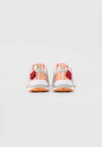 Sports shoes with a white base, orange and gray accents, textured soles, and prominent branding on the heel tab and side panel.
