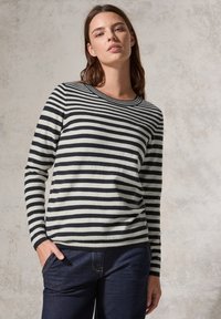 Pull rayé noir et blanc avec des manches longues, un col rond et des poignets côtelés. Associé à un jean noir, doté de poches latérales.
