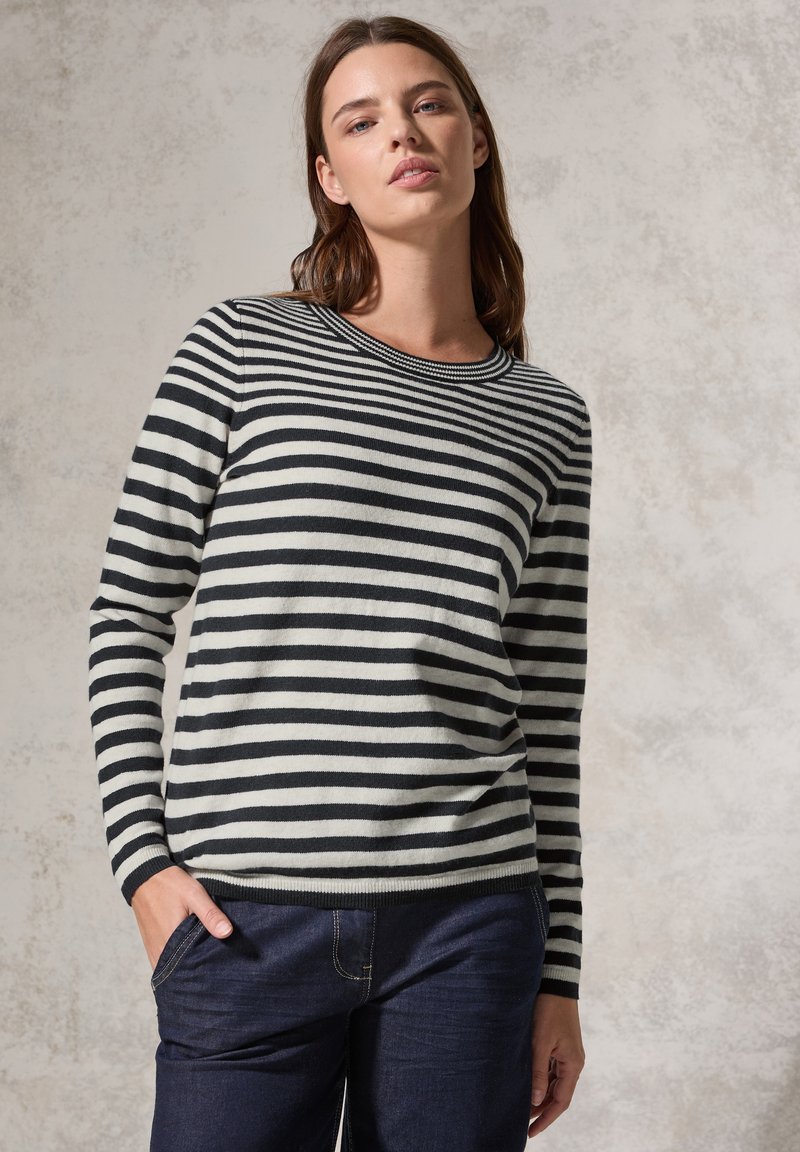 Pull rayé noir et blanc avec des manches longues, un col rond et des poignets côtelés. Associé à un jean noir, doté de poches latérales.