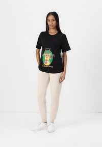 Black short-sleeve t-shirt with colorful reindeer graphic and text, paired with light beige sweatpants and white sneakers. Smooth texture.