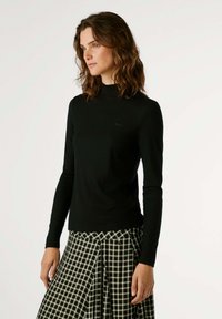 Must mustribbitud turtleneck särk pikade varrukatega, kombineeritud musta ja valge ruudulise plisseeritud seelikuga. Sile tekstuur ja voolav disain.