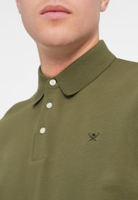 Oliwkowy polo wykonane z fakturowanej bawełny, z dwuprzyciskowym zapięciem i małym czarnym logo na lewej piersi.