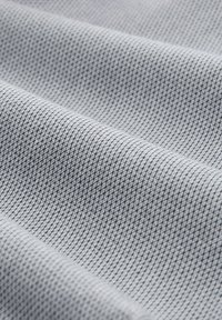 Strukturiertes graues Gewebe mit einem Rautenmuster, das eine sichtbare Webstruktur und eine glatte Oberfläche aufweist. Das Material wirkt leicht und flexibel.