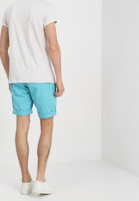 Tyrkysové šortky s ohrnutými manžetami, vyrobené z lehkého materiálu. Nosit s jednobarevným světlým tričkem a bílými teniskami.