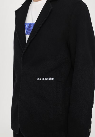 Veste noire avec un motif subtil, dotée d'un col cranté et du logo brodé "LES BENJAMINS" sur le côté. Tissu texturé.