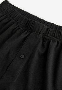 Shorts noirs à taille élastique en tissu doux, dotés d'un bouton noir et d'une poche cousue sur le côté.