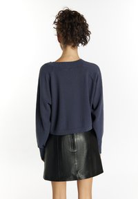 Maglione corto blu navy con un design a maglia testurizzata e spalle scese, abbinato a una minigonna in pelle nera con zip sul retro.