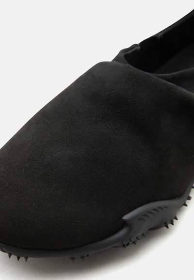 Μαύρο σουέντ παπούτσι εμπρός με στρογγυλεμένη μύτη και σόλα με μικρά ελαστικά αγκάθια για πρόσθετη πρόσφυση.