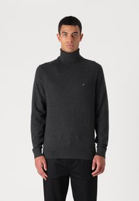 Maglione a collo alto grigio scuro realizzato in tessuto morbido, caratterizzato da un design aderente, maniche lunghe e un piccolo logo sull'area del petto.