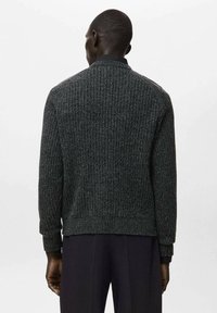 Maglione lavorato a maglia di colore grigio scuro con trama a coste, scollo rotondo e maniche lunghe, con un bordo aderente in vita e dettagli sottili sulle spalle.