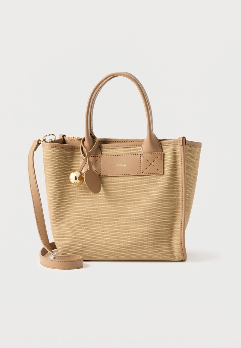 Μπεζ τσάντα tote με υφή, δύο επάνω χειρολαβές και αποσπώμενο λουρί ώμου, με ένα μικρό χρυσό φυλαχτό και διακριτικό ταμπελάκι με το λογότυπο της μάρκας.