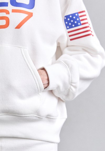 Balts sporta krekls ar lieliem ziliem un oranžiem uzrakstiem, priekšējo kabatu un sarkano un baltu Amerikas karoga uzšuvi uz kreisā piedurknes.