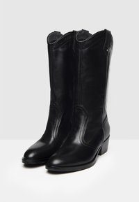 Stivali da cowboy in pelle nera con punta appuntita, stivali di altezza media e decorazioni minimali. Presentano un tacco impilato e linguette laterali.