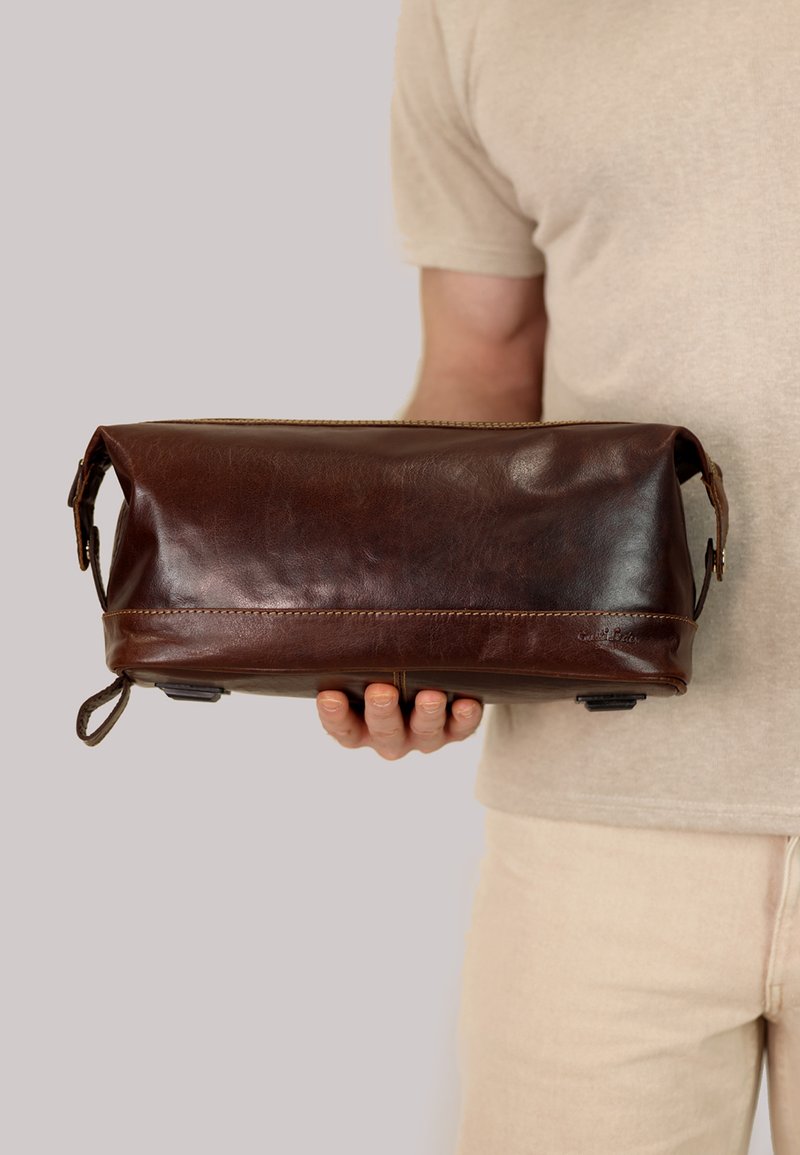 Brown leather bag with a smooth texture, rectangular shape, top zipper closure, and side handles. Features contrast stitching and a small logo.