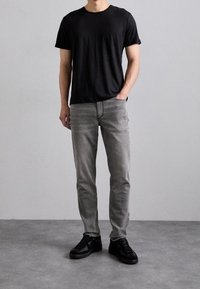T-shirt nera a girocollo, jeans grigi slim-fit e sneakers nere. Il tessuto appare liscio, con un design semplice e senza motivi visibili.