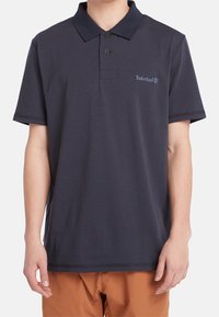 Polo de color azul marino con una textura suave, tapeta de dos botones y el logo de Timberland bordado en el pecho izquierdo. Manga corta.