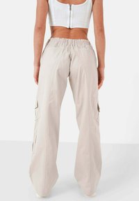Lichtbeige cargobroek met een brede pijp, een elastische tailleband, zijzakken en gestikte details langs de naden. Gladde stoftextuur.
