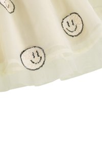 Tilna krilo v svetlo bež barvi z črnimi in bleščečimi nalepkami nasmejancev, z večplastnim naboranim robom za dodatno teksturo.