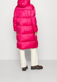 Abrigo acolchado fucsia con capucha, con un diseño acolchado y corte largo. Estilizado con pantalones crema y botas plataforma marrones.