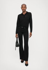 Black long-sleeve polo shirt with a collar, paired with black flared jeans. Accessories include a small black handbag and black pointed-toe heels.