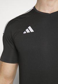 Zwart sportshirt met korte mouwen, gemaakt van vochtafvoerende stof. Beschikt over een V-hals ontwerp en een wit Adidas-logo op de borst.